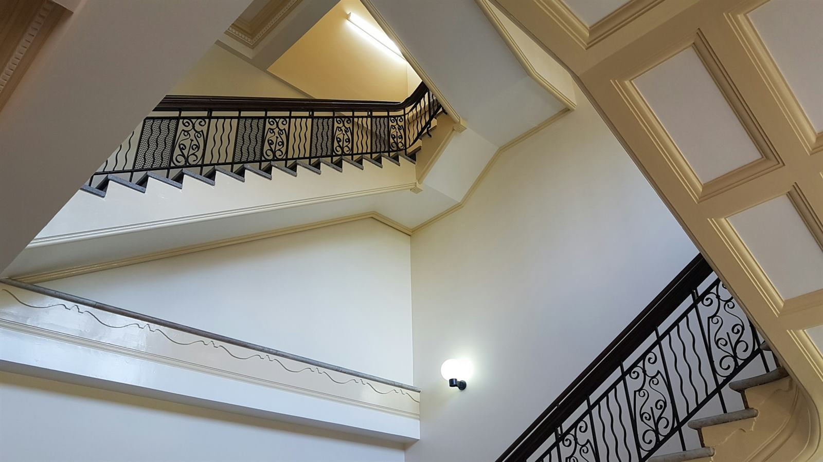 Cage d'escalier avec garde-corps en fer à barreaux verticaux sur plusieurs niveaux